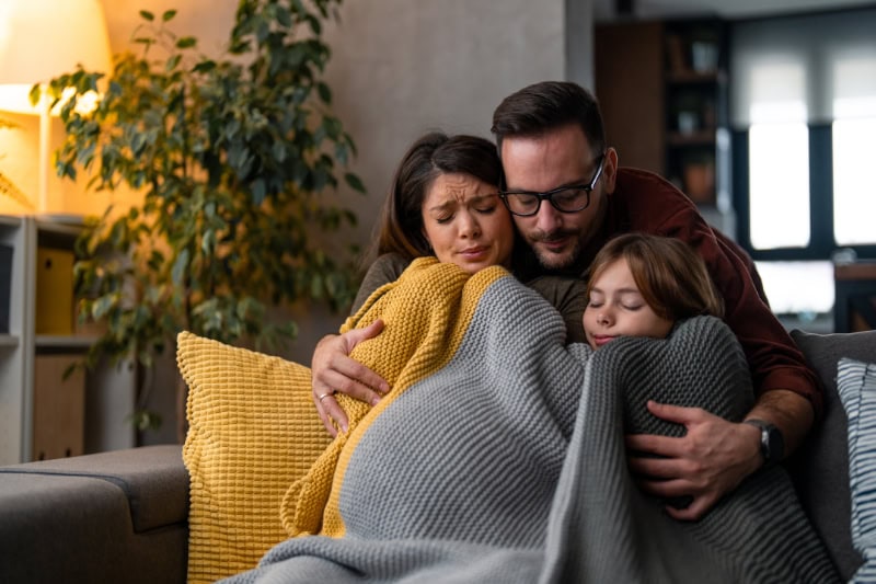 Why Isn’t My Furnace Heating My Entire Home? Family of three, freezing trying to stay warm under a blanket in their living room.