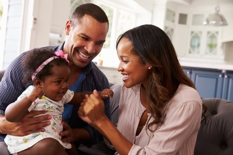 Happy parents playing with baby girl on dad's knee, close-up. Plumber in Metro Denver Area.